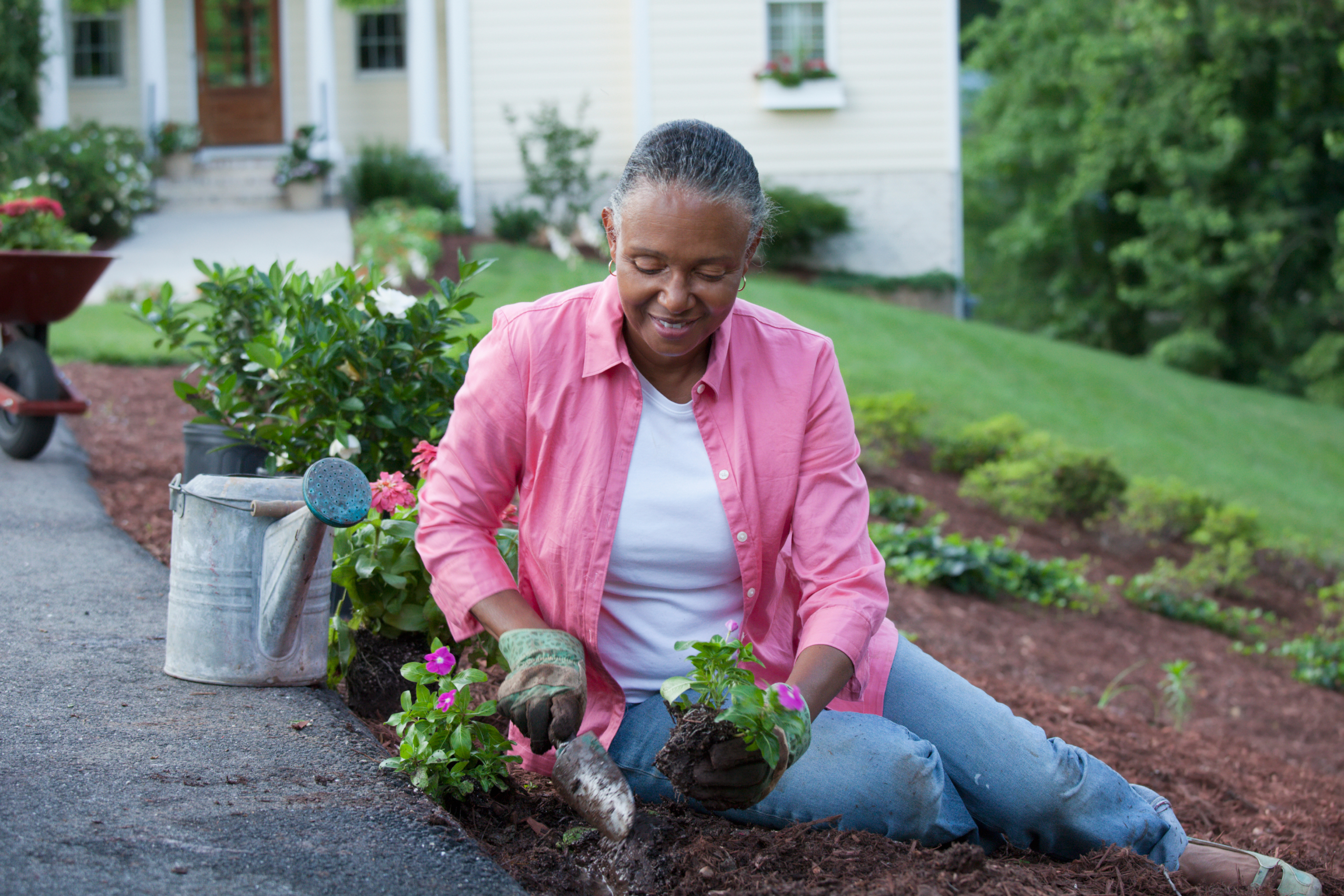 Woman seated in her front yard smiling as she plants annual flowers