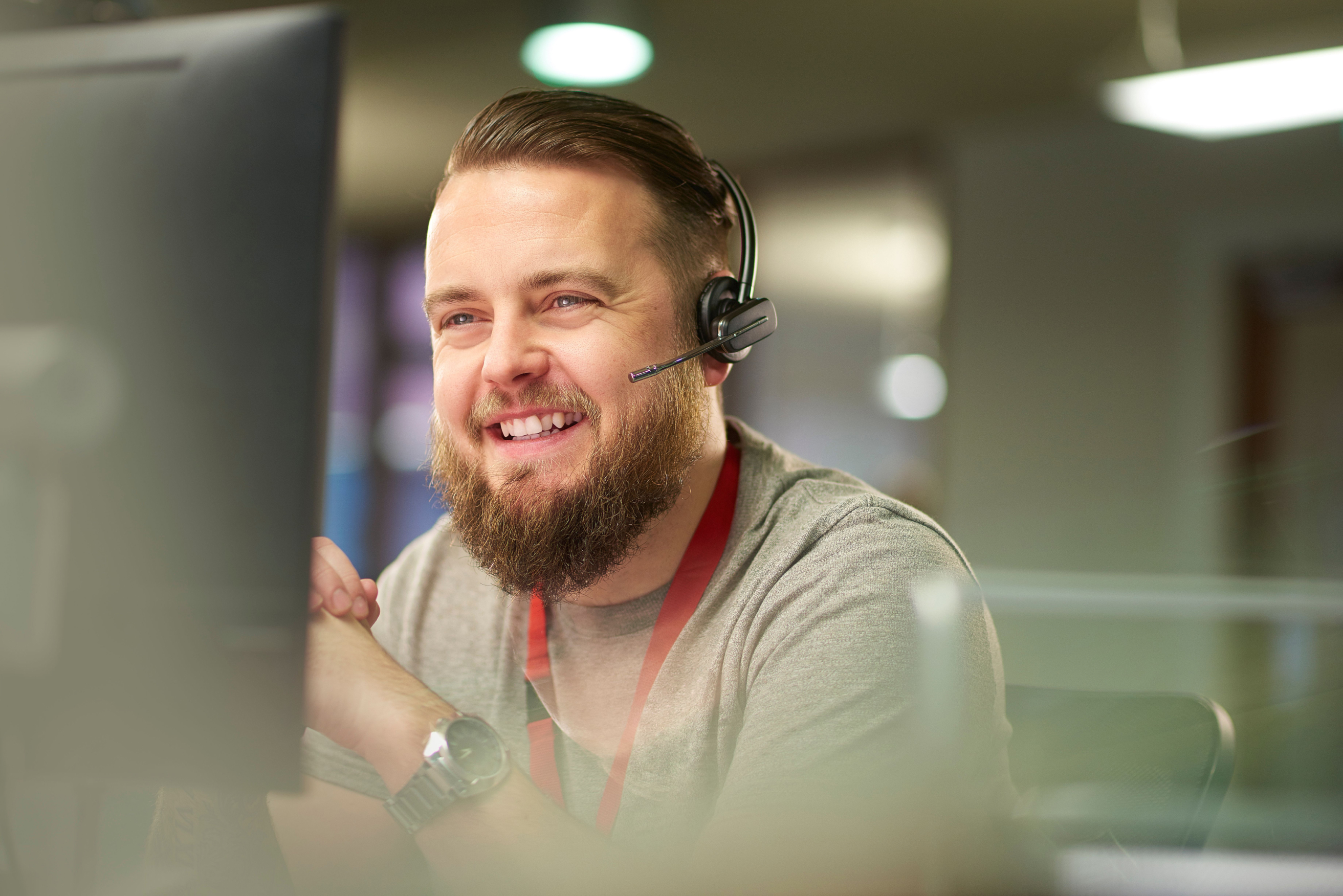 Bearded man seated in office smiling as he talks on his headset