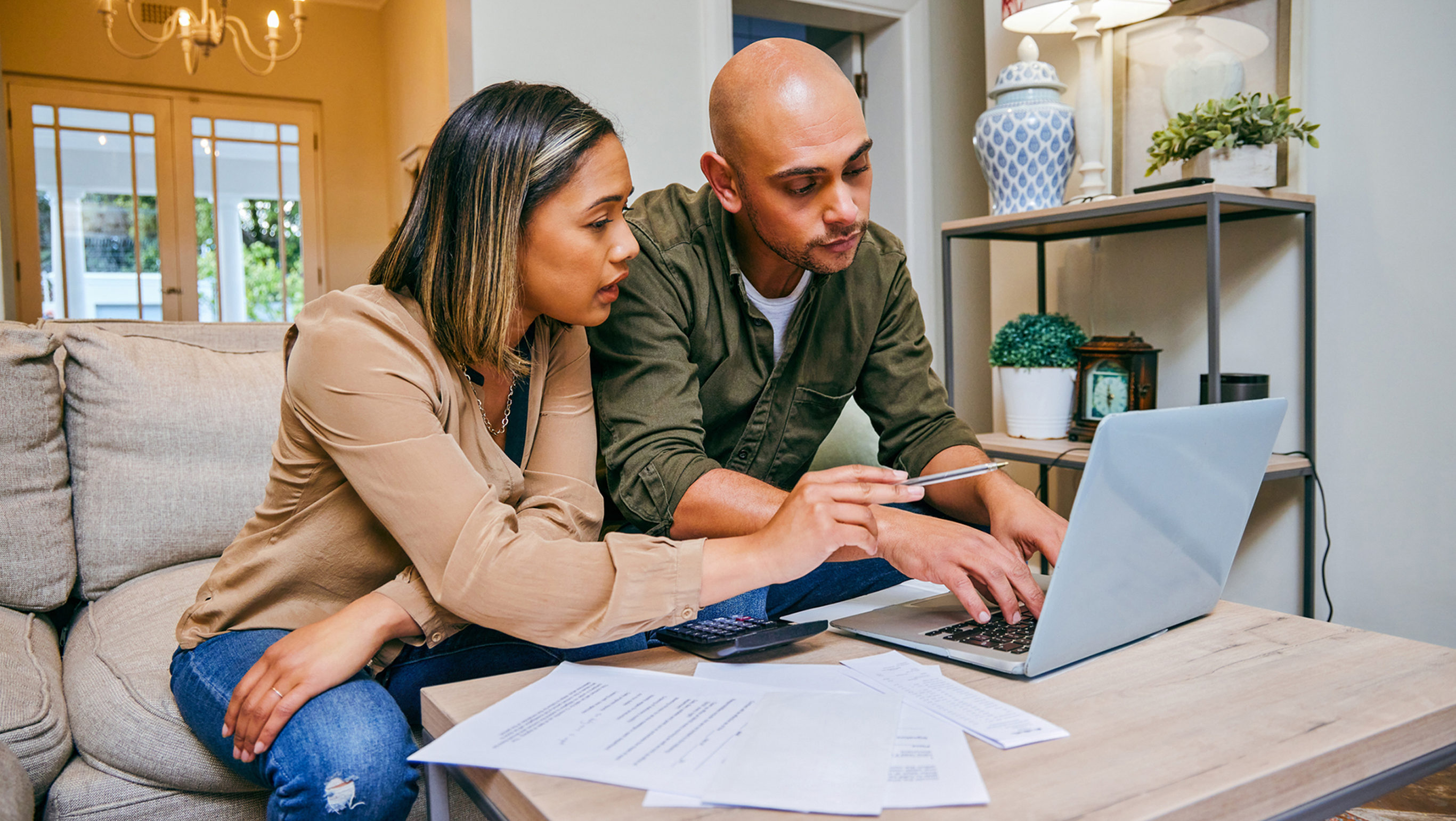 A couple sits at a table looking at a computer and papers.