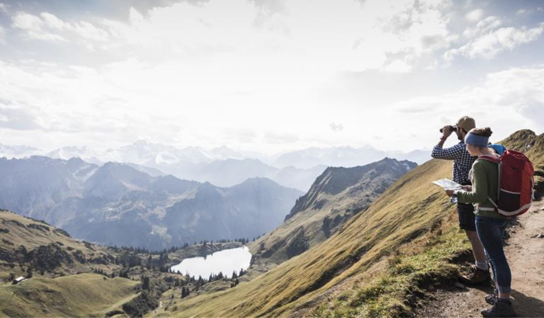 Two hikers looking out over a mountain landscape with a lake.