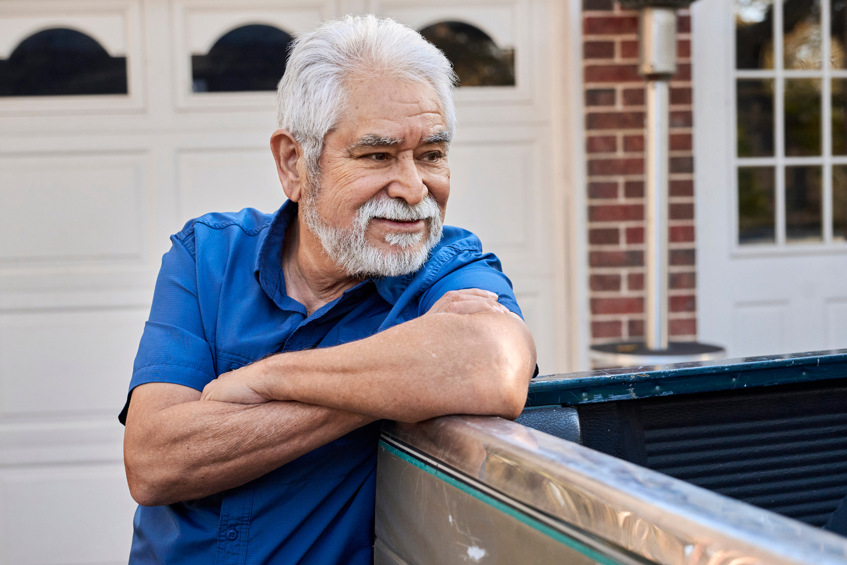 This retirement-age gentleman appears to be in happy thought as he leans on a car parked outside a home’s garage.