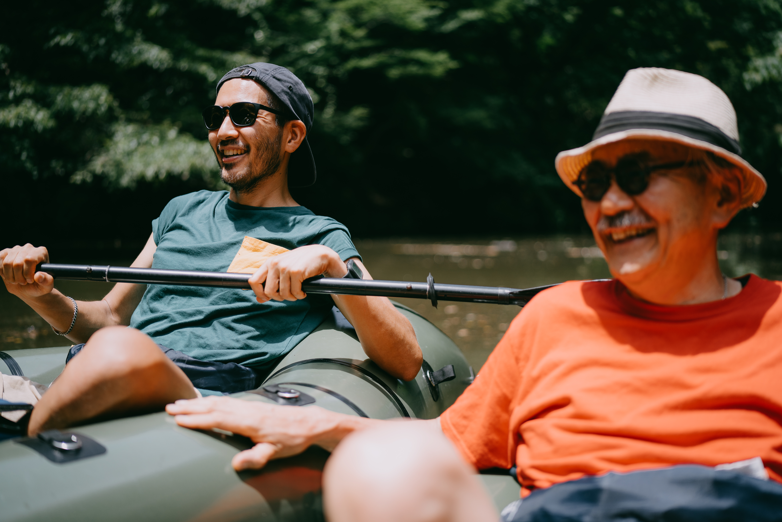 men-rafting_asset50-50_3-2_10grid.png Two men in a boat, smiling and laughing together, enjoying a cheerful moment on the water.
