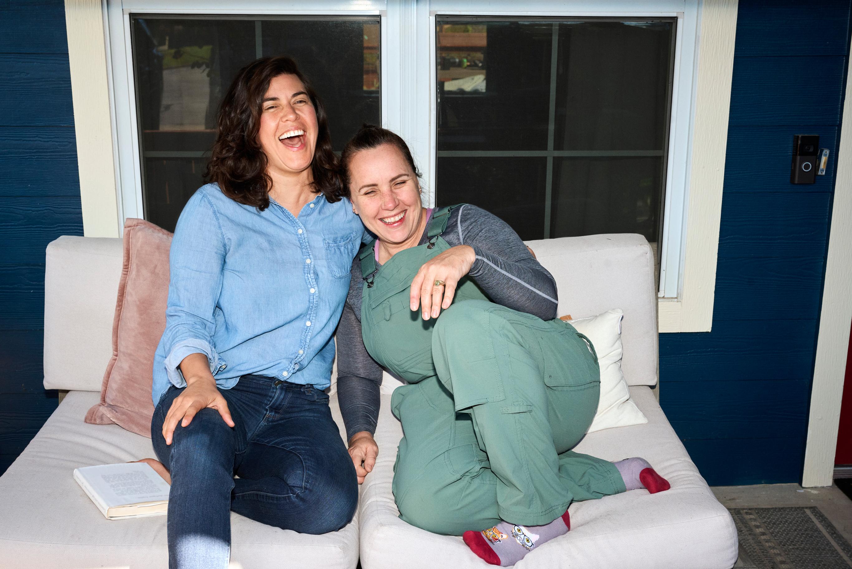 Two women laughing sitting on a couch.
