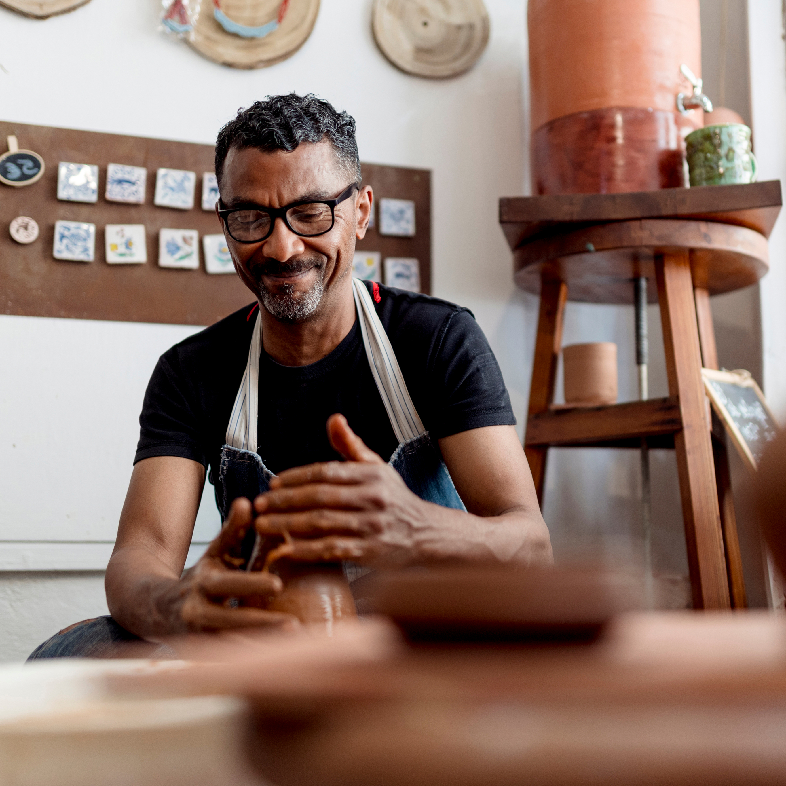 Smiling craftsman in apron working on pottery in his studio