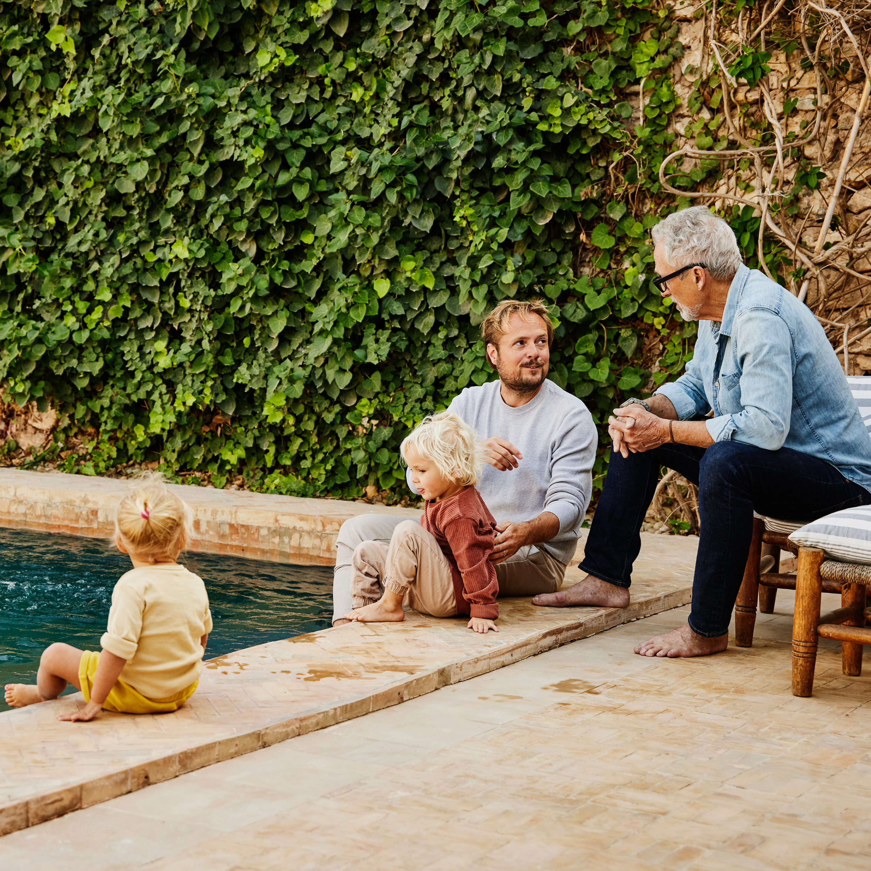 Two men talking poolside as children play, symbolizing family savings and education planning