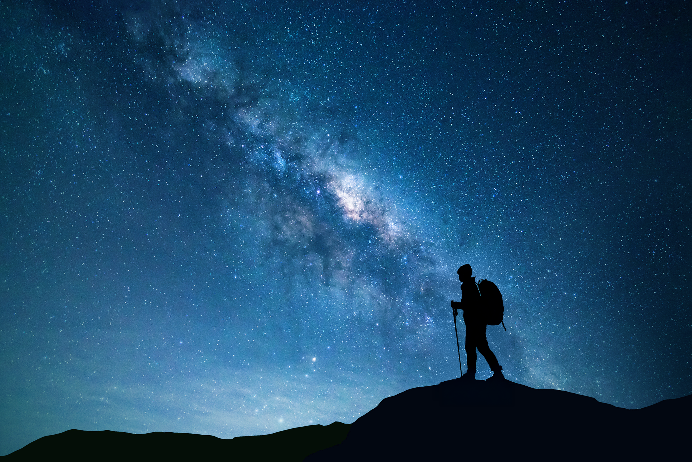 A hiker treks underneath the night sky and stars.