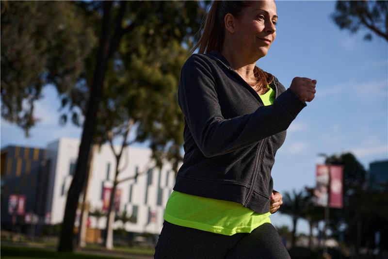 Woman jogging in a sunny park with city buildings in the background